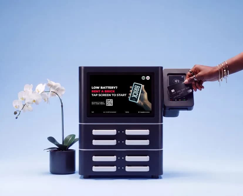 A hand tapping a card on the payment terminal of a Brick Core+ station